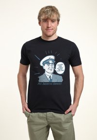 Černé bavlněné tričko s retro grafikou usmívajícího se pilota v bílém klobouku, s textem "Děkujeme, že jste letěli s Pan Am!"