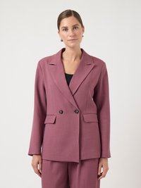 Blazer croisé en tissu mauve doux avec revers crantés, deux poches avant et boutons noirs. Porté sur un haut noir.