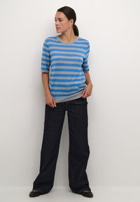 Pull en tricot bleu et gris à rayures, avec des manches courtes, associé à un jean large bleu foncé. Design décontracté avec une coupe ample.