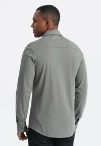 Graues langärmliges Hemd mit Kragen, das eine glatte Textur und knöpfbare Manschetten aufweist. Die Rückseite zeigt ein präzises Nahtdesign und einen abgerundeten Saum.