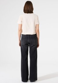 Camiseta de algodón crema con mangas cortas y pantalones vaqueros de pierna ancha negros. Los vaqueros presentan un diseño clásico de cinco bolsillos y una textura ligeramente descolorida.