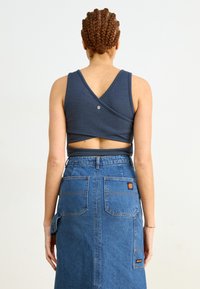Navy blue cropped top with a crisscross back design, ribbed texture, and small metallic button, paired with a high-waisted denim skirt.