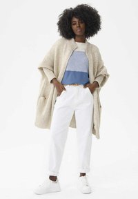 Beżowy sweter z dzianiny, jasnoniebieski sweter w paski, białe spodnie i białe trampki. Luźny krój z kieszeniami w swetrze.