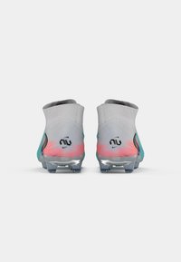 Crampoane de fotbal gri cu un design la gleznă, având accente roz și teal, un material texturat și cu știfturi transparente pe un fundal alb.