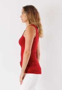 Top senza maniche rosso realizzato in tessuto elasticizzato, design aderente con scollatura a barca, abbinato a pantaloni bianchi attillati.
