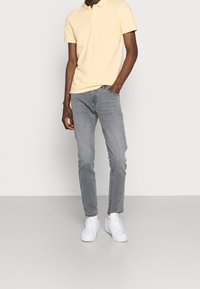 Gul kortärmad polo med vita kragdetaljer, kombinerad med ljusgrå slim fit-jeans och vita sneakers. Enkelt design och rena linjer.