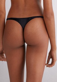 Zwarte string onderbroek met een gladde afwerking, voorzien van een dunne tailleband en minimale achterkant bedekking, ontworpen voor een naadloze uitstraling.