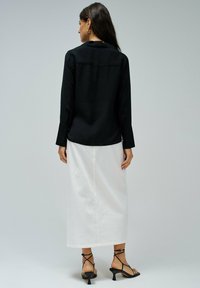 Camisa negra de manga larga con cuello, combinada con una falda blanca hasta los tobillos. El modelo lleva sandalias negras con tiras. Diseño simple y tejido texturizado.