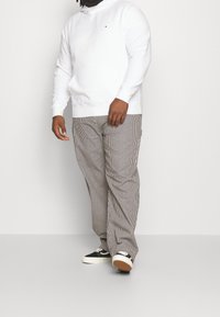 Sudadera blanca con capucha, pantalones a rayas en beige y marrón, con un corte relajado. Zapatillas negras con acentos blancos y suelas de goma.