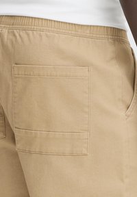 Khaki pants with an elastic waistband, featuring a back pocket and smooth texture. Stitched seams visible, no distinct patterns or accents.