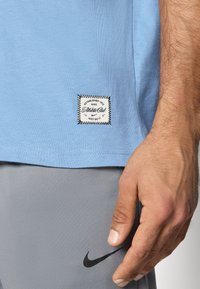 Ανοιχτό γαλάζιο βαμβακερό T-shirt με ορθογώνια μαύρη και λευκή ετικέτα κοντά στο τελείωμα, που αναγράφει "Established 1971 Nike Athletic Club Just Do It".