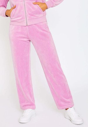 Rosa Fleece-Sweatpants mit lockerer Passform, sichtbar weicher Textur und elastischem Bund. Kombiniert mit weißen Sneakers für einen lässigen Look.
