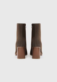 Bottines en daim marron avec un bout carré, fermeture éclair et talon empilé. Détails texturés le long des coutures, finition lisse.