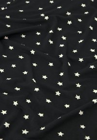 Svart tyg med små vita femuddiga stjärnor jämnt utspridda, som visar mjuka veck och textur.