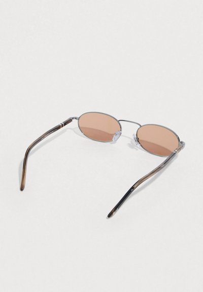 Καφετί οβάλ γυαλιά ηλίου με λεπτό μεταλλικό πλαίσιο και καφέ άξονες από ακρυλικό με ριγέ σχεδιασμό. Διαφανείς ρινοβάτες για άνεση.