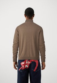 Brun stickad tröja med hög krage, med ribbade ärmslut och nederkant. I kombination med blå jeans som har en röd grafisk design.