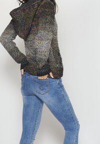 Gebreide hoodie met een veelkleurig textuurpatroon; grijs en zwarte tinten. Gecombineerd met een aangesloten blauwe jeans met decoratieve achterzakken.