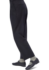 Unterschenkel mit schwarzen, gerade geschnittenen Hosen, grauen, gerippten Socken und schwarzen Mary-Jane-Schuhen mit Schnallenriemen.