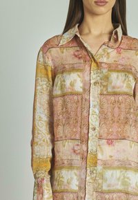 Camisa de manga larga abotonada en tela ligera, con patrones florales y barrocos en múltiples colores, y un cuello con solapa.