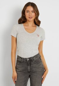Gray short-sleeve T-shirt with a V-neck and a small red triangular logo on the left chest, paired with dark gray high-waisted jeans.