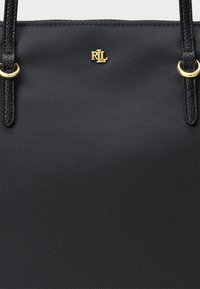 Juodas tote tipo krepšys su tekstūruota medžiaga, pasižymintis auksinėmis detalėmis ir logotipu. Dviejų rankenų ir paprasto, struktūrizuoto dizaino.