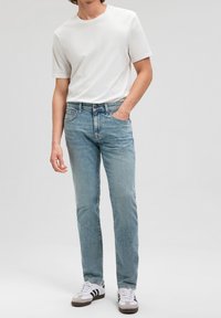 Jeans de denim azul claro con corte recto, combinados con una camiseta blanca básica. Diseño minimalista y un corte clásico, llevados con zapatillas blancas.