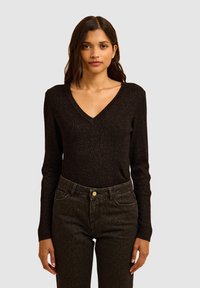 Zwarte lange mouwen trui met V-hals, met een geribbelde textuur en subtiele metalen draadjes, gecombineerd met donkere jeans met luipaardprint.