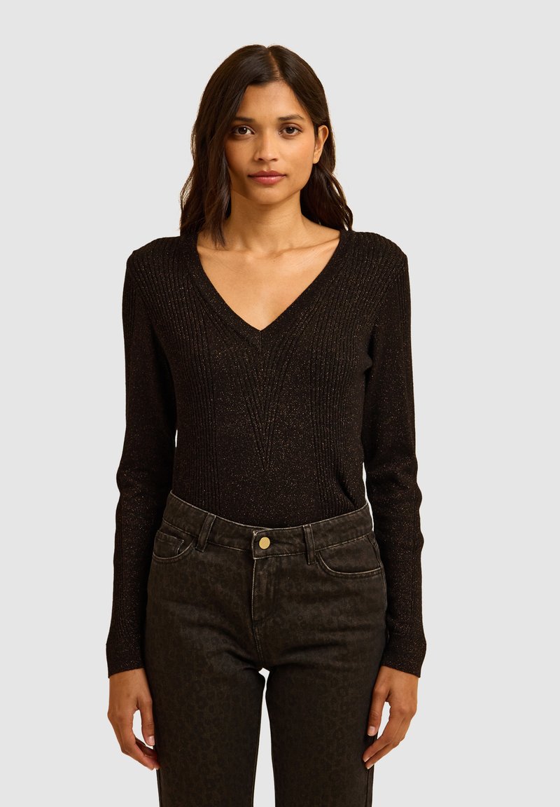 Zwarte lange mouwen trui met V-hals, met een geribbelde textuur en subtiele metalen draadjes, gecombineerd met donkere jeans met luipaardprint.