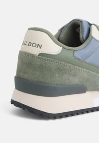 Zapatilla verde y azul con un upper de ante texturizado, acentos contrastantes, una suela acolchada y la marca "SILBON" cerca del talón.