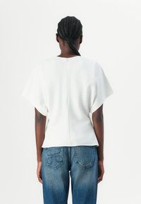 White short-sleeve top with a loose fit, smooth texture, and back zipper detail, paired with high-waisted blue jeans featuring embroidered pockets.