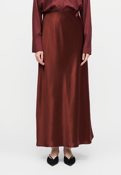 Długa, bordowa satynowa spódnica o gładkiej fakturze i płynącej sylwetce, zestawiona z dopasowaną koszulą z długim rękawem oraz czarnymi spiczastymi butami.