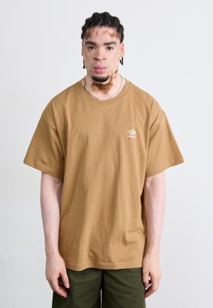 Brun oversized t-shirt lavet af bomuld, med korte ærmer og et lille hvidt logo på venstre bryst. Simpelt design, ingen mønstre eller detaljer.