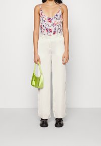 Floral camisole in light fabric, cream wide-leg trousers, and a glossy green handbag. Black shoes with a chunky sole.