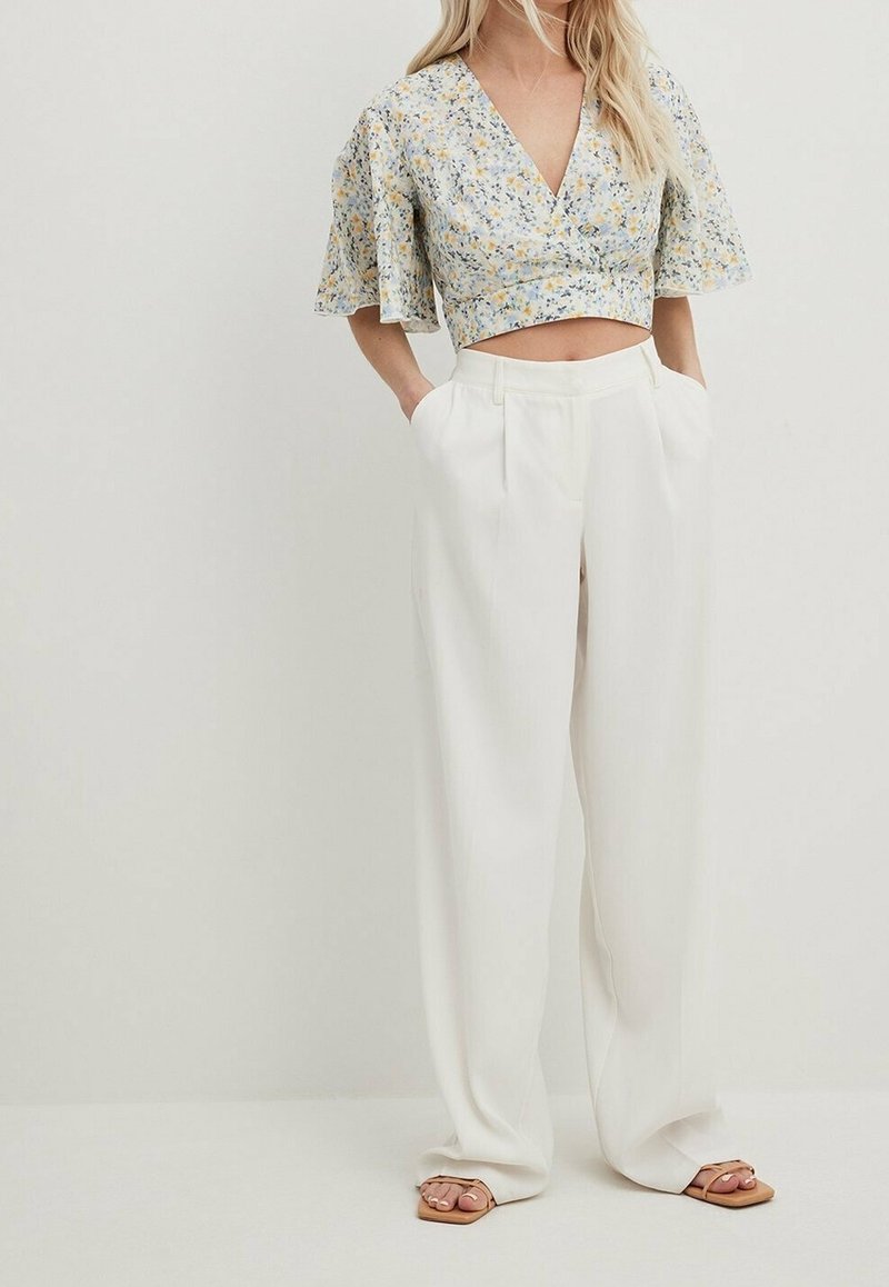 Top court floral avec un décolleté en V profond, associé à un pantalon blanc taille haute et large. Présente des manches bouffantes et une texture douce.