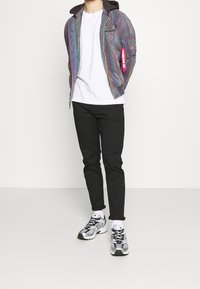 Irydescencyjna kurtka z zamkiem, z kapturem, czarne spodnie i srebrne buty sportowe. Posiada logo na klatce piersiowej i różową metkę na zamku.