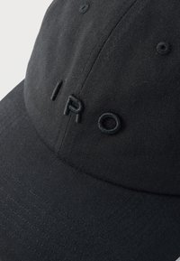 Gorra de béisbol negra con letras bordadas en relieve negras que dicen "IRO" en el panel frontal, con ojales de ventilación cosidos.