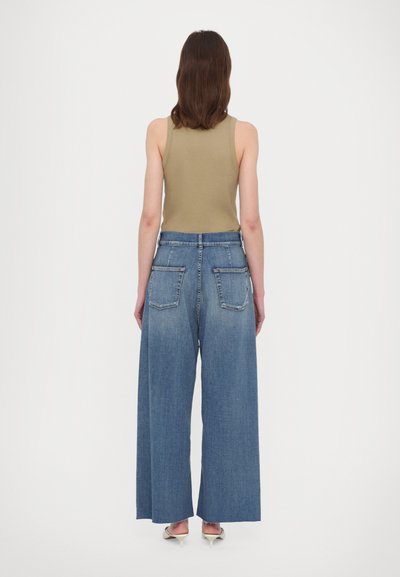 Wide-leg blue denim jeans with two back pockets, paired with a fitted olive green tank top. The fabric has a soft texture.