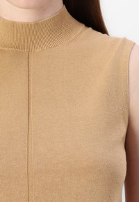 Beżowy bezrękawnik z wysokim prążkowanym kołnierzem, wykonany z miękkiej dzianiny, z detalem centralnego szwu. Gładka faktura.