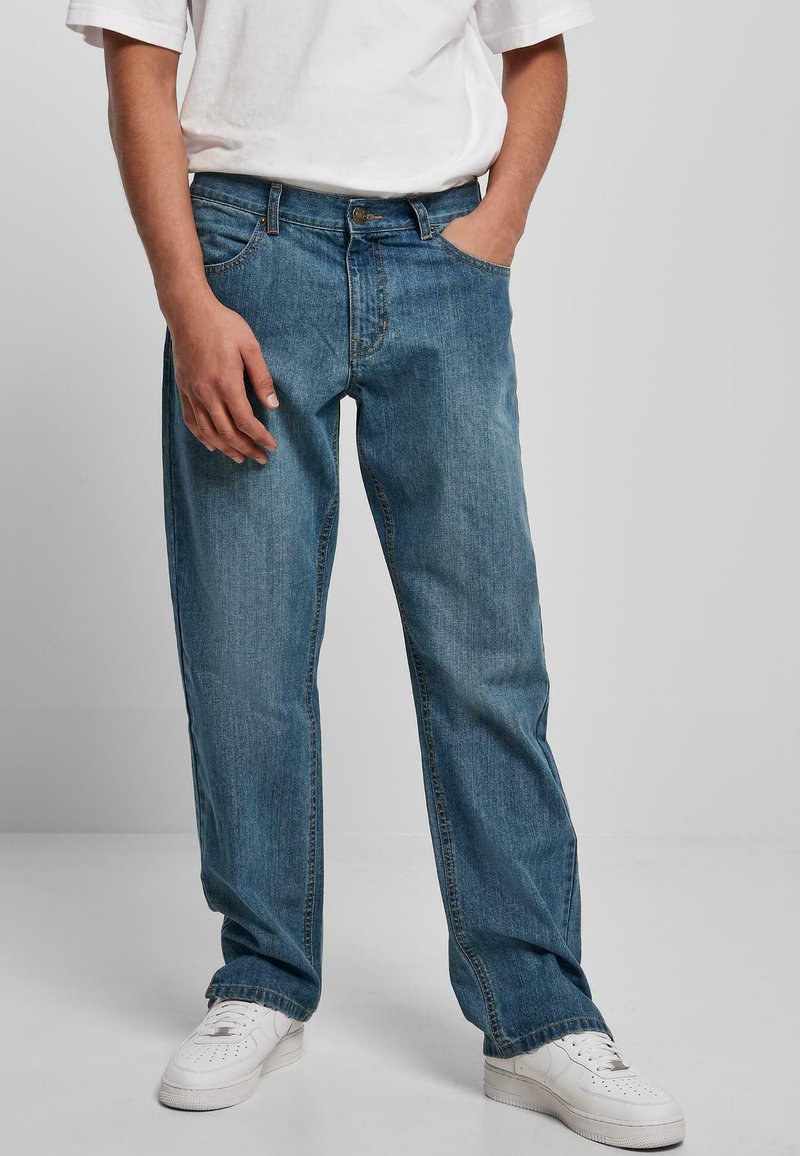 Heled sinised denim teksad, millel on mugav lõige, sirged sääred, viis taskut ja peene pleekimine, koos valgete tossudega.