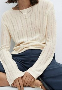 Kermanvärinen neulepusero, jossa pitkät hihat, avoin pääntie ja resorikuvio. Yhdistetty tummansinisiin, leveälahkeisiin housuihin.