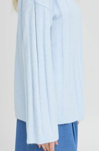 Hellblauer Pullover mit gerippter Textur, langen Ärmeln und tailliertem Saum. Kombiniert mit hellblauen Hosen, die ein sanftes, gemütliches Aussehen zeigen.