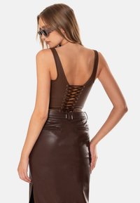 Top in ecopelle marrone con schiena bassa e dettaglio con lacci, abbinato a una gonna alta in vita marrone coordinata con fessure frontali.