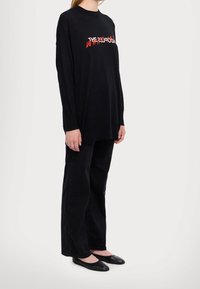 Czarna koszulka z długim rękawem z czerwono-białym napisem, w połączeniu z czarnymi spodniami i czarnymi balerinami. Prosty, luźny krój i jednolity kolor.