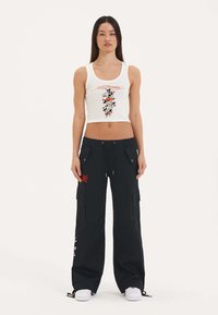 Hvid cropped tanktop med grafisk print, parret med sorte cargo bukser med lommer, justerbare bånd og røde detaljer. Hvide sneakers.