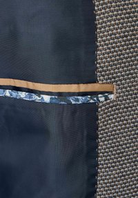 Oberbekleidung aus strukturiertem braunem Hahnentrittmuster, mit einem einfarbigen navyblauen Abschnitt und einem kontrastierenden floral gemusterten Innentaschenfutter.
