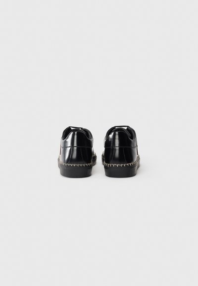 Schwarze Lacklederschuhe mit abgerundeter Form, versehen mit einer kontrastierenden genähten Sohle und einem glatten Finish. Keine sichtbare Markenkennzeichnung auf der Rückseite.