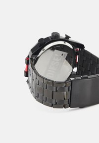 Schwarze Metalluhr mit einem Gliederarmband, runder Gehäuseform, roten Akzenten, Mineralglas und wasserdicht bis 5 bar. Markenlabel sichtbar.