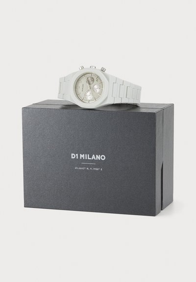 White silicone watch on a black box. Watch features a round face, silver accents, three sub-dials, and a textured strap. Brand name displayed.