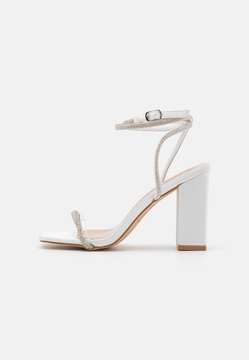 Sandale blanche à talon haut, avec un talon bloc, une bride à la cheville et une lanière à l'avant ornée de petits strass étincelants.
