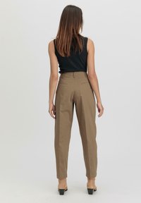 Hoge taille khaki broek met zijzakken, rechte pijpen en een zachte textuur. Gecombineerd met een zwarte mouwloze top en hoge hakken.